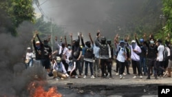 Anti-coup protesters flash the three-finger salute, a symbol of resistance, as they are confronted by security forces in Thaketa township, Yangon, Myanmar, March 27, 2021. 