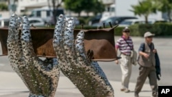 Pedestrians walk by artist Heath Satow's sculpture "Reflect," made with a damaged, rusted I-beam from the collapsed World Trade Center buildings, outside the Rosemead, California, city hall plaza. Aug. 26, 2016.