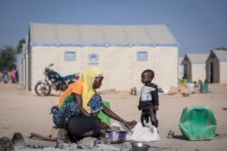 FILE - In this photo taken on Dec. 10, 2019 a displaced Burkinabe woman and child prepare food, in the Pissila town camp, near Kaya, Burkina Faso.
