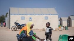 FILE - In this photo taken on Dec. 10, 2019 a displaced Burkinabe woman and child prepare food, in the Pissila town camp, near Kaya, Burkina Faso. 