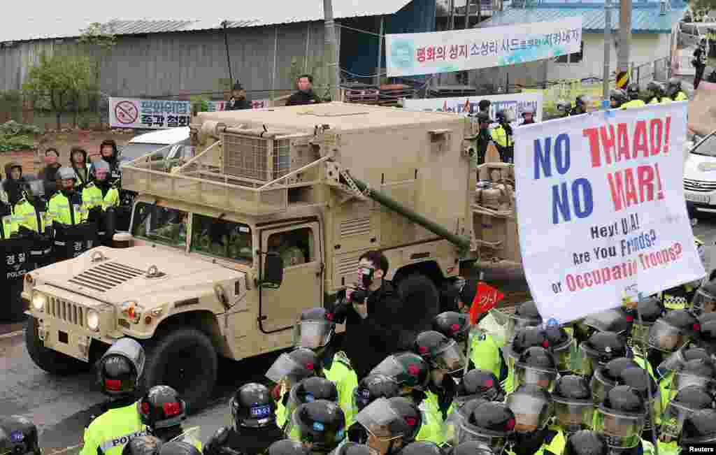 美国驻韩国部队提供的图片显示，卡车运送萨德系统的导弹发射器和其他设备，抵达美国在韩国的空军基地。在军人的后面有韩国示威者，举着标语&ldquo;不要萨德！不要战争！&rdquo;（2017年3月6日）。