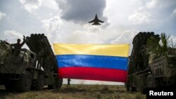 A Russian-made Sukhoi Su-30MKV fighter jet of the Venezuelan Air Force flies over a Venezuelan flag tied to missile launchers.