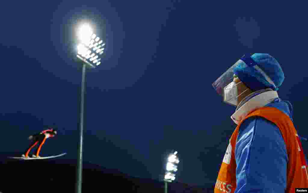 A member of the medical crew watches Andrei Feldorean of Romania in action during men&#39;s ski jumping at the 2022 Beijing Olympics, at the National Ski Jumping Centre, Zhangjiakou, China.