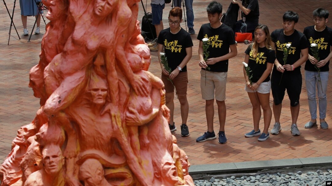 FILE - University students place flowers on the "Pillar of Shame" statue, a memorial for those injured and killed in the 1989 Tiananmen Square crackdown, at the University of Hong Kong, June 4, 2018.