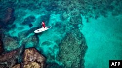 A man dressed in Santa Claus clothes rides on a standup paddle board in Lebanon&#39;s northern coastal city of Batroun.