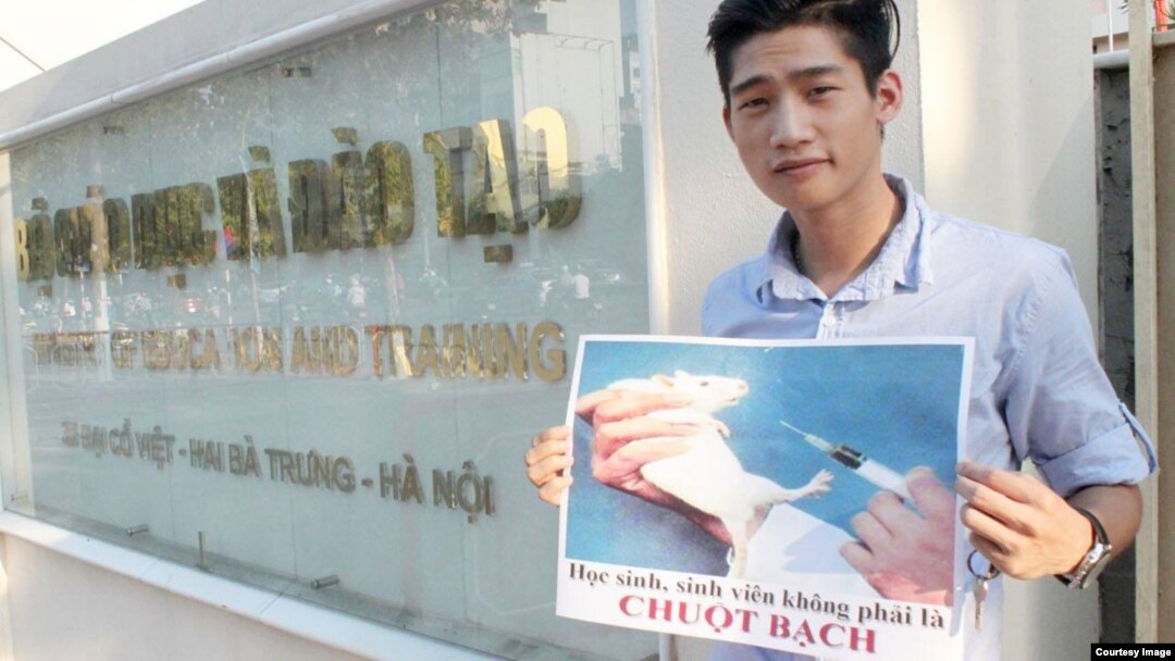 Nguyễn Thành Nhân cầm tấm biển: “Học sinh, sinh viên, không phải là chuột bạch” trước cổng Bộ Giáo dục và Đào tạo. 