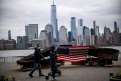 Orang-orang memakai masker saat berjalan di dekat tugu peringatan 11 September di tengah pandemi COVID-19, dengan latar belakang Gedung "One World Trade Center" dan cakrawala New York terlihat dari Exchange Place, di New Jersey (REUTERS)