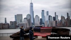 People wear face mask as they walk near a 9-11 memorial during the coronavirus disease (COVID-19) pandemic, while the One World Trade Center and New York skyline are seen from Exchange Place, in New Jersey