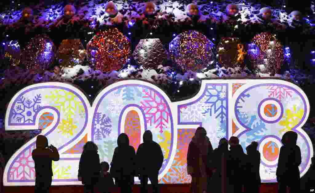 People stand in front of a 2018 sign in Octyabrskaya Square decorated to mark the upcoming Christmas and New Year celebrations in Minsk, Belarus, Friday, Dec. 22, 2017. (AP Photo/Sergei Grits)