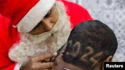 2023年12月31日，在印度艾哈迈达巴德的一家理发店里，一名理发师身穿圣诞老人服装，为客户剪“2024”胡须，迎接新年。（路透社）