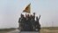 FILE - U.S.-backed Syrian Democratic Forces fighters stand on their pickup as the flash victory signs after battling the Islamic State militants, northeast Syria, July 26, 2017.