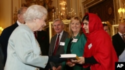 Malala Yousafzai, derecha, entrega una copia de su libro a la reina Elizabeth de Inglaterra durante una recepción en honor a la juventud celebrada en palacio.