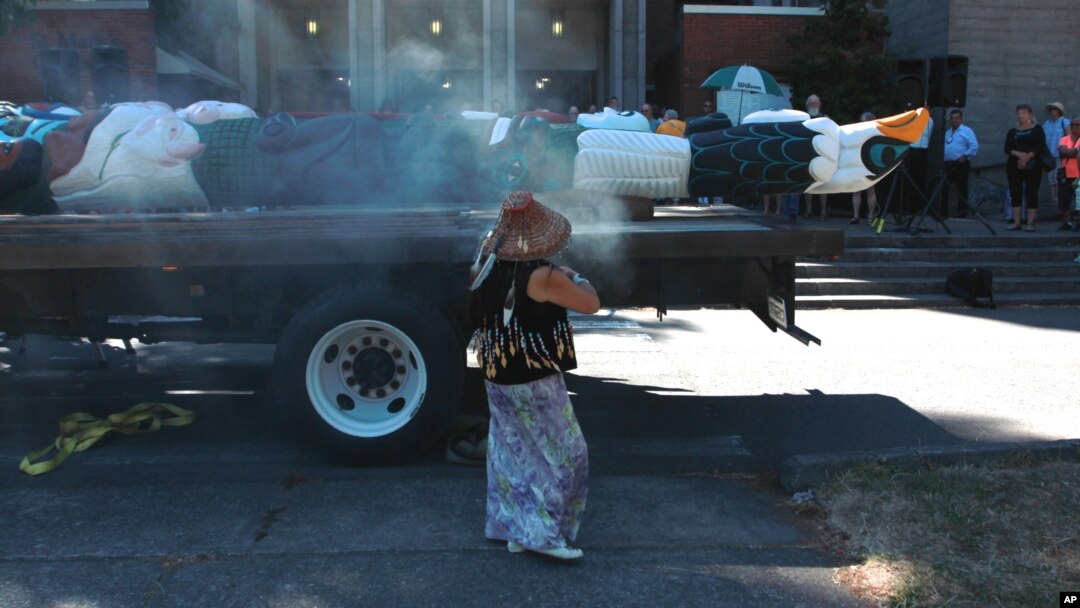 Linda Soriano of the Lummi Nation performs a smudge ceremony at Saint Mark's Episcopal Cathedral in Seattle, fanning smoke from burning sage with eagle feathers onto a totem pole, Aug. 25, 2016. 