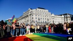 FILE - People gather at a giant rainbow flag during a rally in front of the Hungarian Parliament in Budapest, Hungary, June. 14, 2021, calling on lawmakers to reject legislation banning any content portraying homosexuality or sex reassignment to minors. 