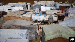 FILE - Syrian refugees stand outside their tents at a Syrian refugee camp in the town of Hosh Hareem, in the Bekaa valley, east Lebanon, Oct. 28, 2015. 