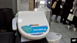 Shoppers stand near a smart toilet seat cover on display at a shopping mall in Beijing, China, April 20, 2016. The Chinese government's latest plan to perk up its slowing economy is based on the humble rice cooker and luxury toilet seats. 