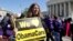 FILE - Holding a sign saying "We Love ObamaCare," a supporter of health care reform rallies in front of the Supreme Court in Washington, D.C., March 27, 2012.