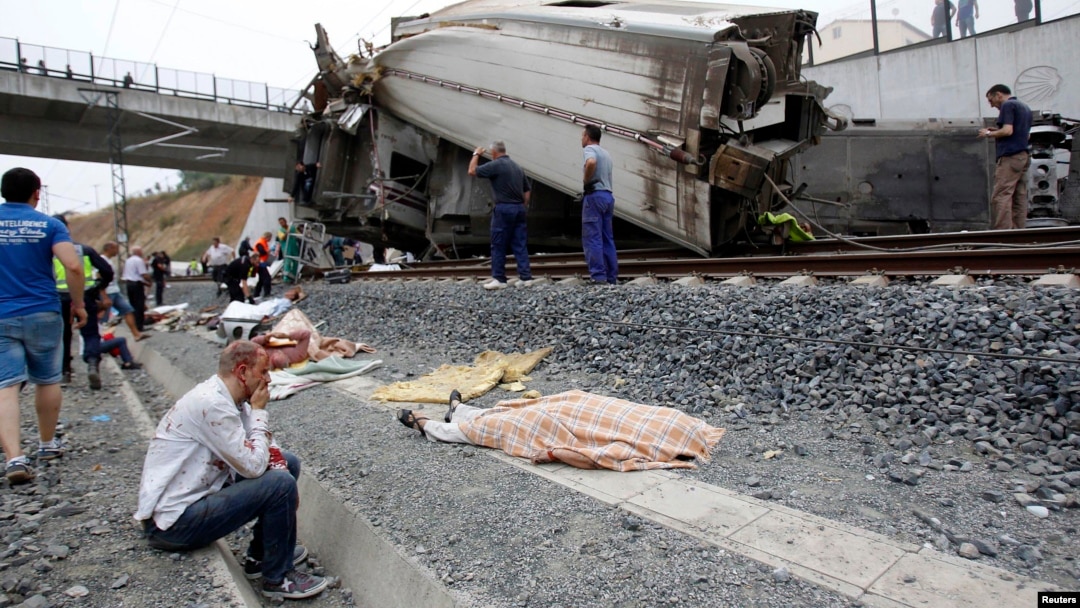 A wounded victim sits next to a body covered with a blanket after a train crashed near Santiago de Compostela, northwestern Spain, July 24, 2013.