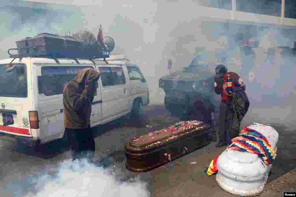 Supporters of former Bolivian President Evo Morales take cover from tear gas in La Paz while carrying coffins of people they say were killed during recent clashes with security forces in Senkata, Nov. 21, 2019. 