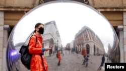 A person wearing a face mask is reflected in an art work entitled "A=V" by Ben Cullen Williams, amid the coronavirus outbreak, in Covent Garden, London, Britain.