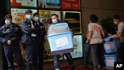 Pekerja membawa beberapa barang bukti berjalan melewati petugas polisi di luar kantor "Stand News" di Hong Kong Rabu, 29 Desember 2021. (Foto: AP)