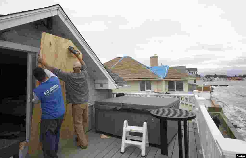 Patrick Smith dan Ed Morrissey (kanan) memasang papan di rumah kawan mereka untuk melindungi diri dari Badai Sandy yang tiba di Milford, Connecticut, 28/10.