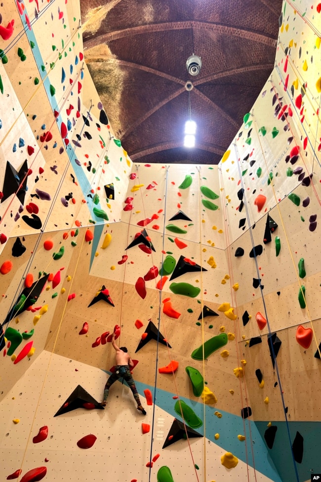 A climber scales a wall in the repurposed Saint-Antoine church in Brussels, Belgium, Wednesday, June 21, 2023. (AP Photo/Sylvain Plazy)