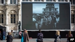 People watch former President Jacques Chirac on a giant screen set up at the Paris town hall, Sept. 27, 2019. Mourners signed memory books and flags were lowered in honor of the late president.