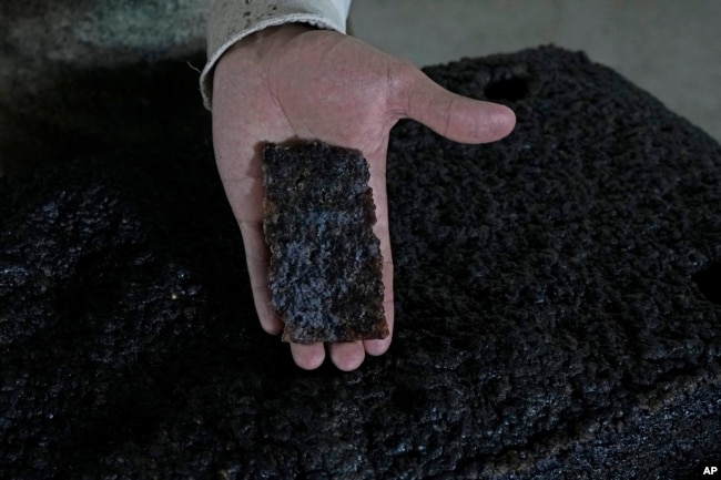 A worker shows a piece of a processed rubber plate taken for sample control at a rubber industrial plant of the cooperative called Cooperacre, in Sena Madureira, Acre state, Brazil, Friday, Dec. 9, 2022. (AP Photo/Eraldo Peres)