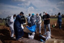 FILE - Family members and volunteers from the Saaberie Chishty Society lower the body of a COVID-19 victim into a grave at the Avalon cemetery in Lenasia, South Africa, Jan. 4, 2021.
