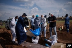FILE - Family members and volunteers from the Saaberie Chishty Society lower the body of a COVID-19 victim into a grave at the Avalon cemetery in Lenasia, South Africa, Jan. 4, 2021.