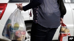 FILE - A shopper leaves a supermarket with goods in plastic bags in Christchurch, New Zealand, Aug. 10, 2018. 