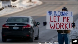 Un trabajador de la Agencia de Protección Ambiental de EEUU (EPA, por sus siglas en inglés) afectado por el cierre parcial del gobierno protesta con un cartel ante las oficinas del senador Mitch McConnell, en Park Hills, Kentucky.