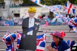 Una persona en el Mall de Londres junto a un recorte de cartón del Rey Carlos III el viernes 5 de mayo de 2023, un día antes de la coronación. (Foto AP/Jon Súper)
