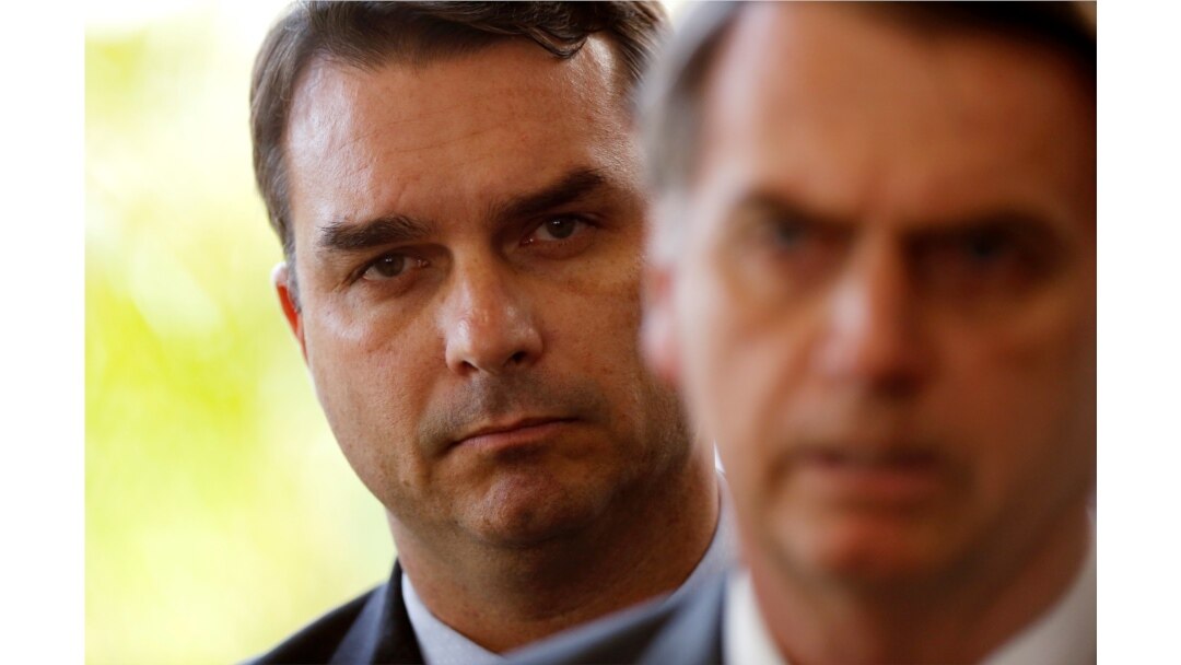 FILE - Flavio Bolsonaro, son of Jair Bolsonaro, is seen behind him at the transition government building in Brasilia, Nov. 27, 2018.
