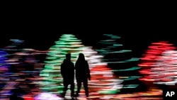 In this Dec. 12, 2019, photo taken with a long exposure, people are silhouetted against a Christmas display, at a park in Lenexa, Kan.