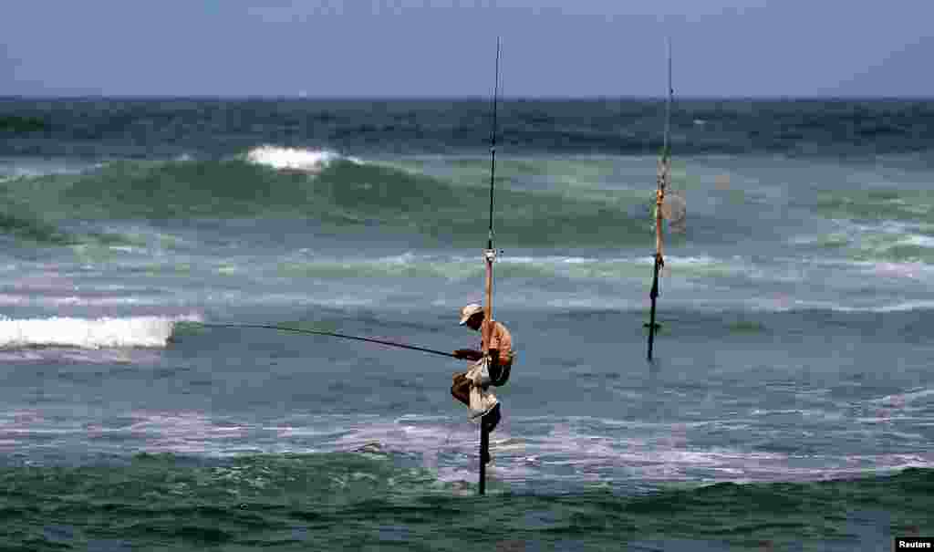 A fisherman catches fish as he sits atop a stilt in the sea in Koggala, Sri Lanka.