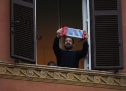 A man plays accordion as he looks out of an apartment window as part of a flashmob organized to raise morale during Italy's coronavirus crisis in Rome, March 13, 2020.