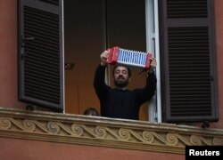 A man plays accordion as he looks out of an apartment window as part of a flashmob organized to raise morale during Italy's coronavirus crisis in Rome, March 13, 2020.