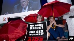 People protest in front of the stage as Sen. Mike Enzi is seen on a giant video screen during the XIX International AIDS Conference in Washington, July 25, 2012.