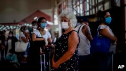 Tourists wearing masks as a precaution against the spread of the new coronavirus, wait in line for their flights home, at the Jose Marti International Airport in Havana, Cuba, Monday, March 23, 2020.