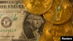 En esta ilustración tomada el 25 de junio de 2021, se muestran representaciones de bitcoin en moneda virtual sobre un billete de dólar estadounidense a través de un vidrio roto.