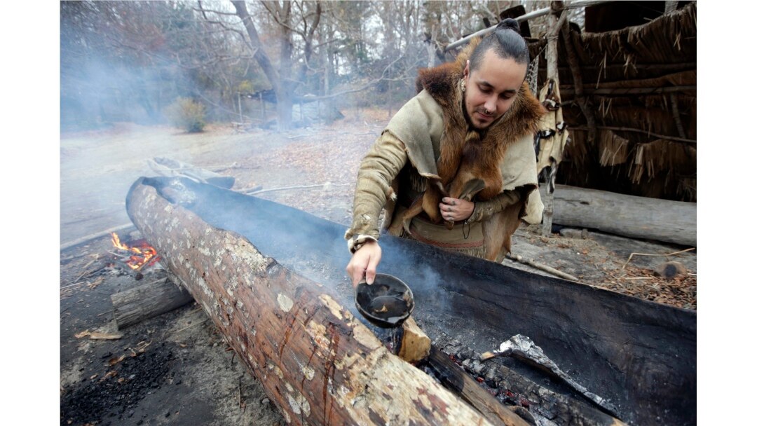 Mashpee Wampanoag Phillip Wynne pours water to control fire and temperatures while making a boat, from a tree at the Wampanoag Homesite at Plimoth Plantation, in Plymouth, Mass.