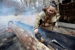 Mashpee Wampanoag Phillip Wynne pours water to control fire and temperatures while making a boat, from a tree at the Wampanoag Homesite at Plimoth Plantation, in Plymouth, Mass.
