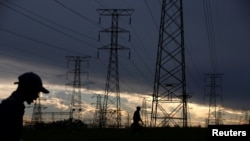 FILE - Men walk past electricity pylons as they return from work in Orlando, Soweto township, South Africa, March 18, 2019. 