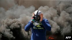 Seorang pria Palestina mengenakan topeng gas di dekat tumpukan ban yang terbakar dalam sebuah unjuk rasa di kota Ramallah, di Tepi Barat, tanggal 6 April 2018 (foto: AFP Photo/Abbas Momani)