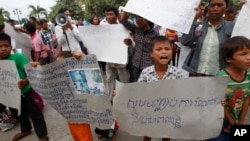 FILE - A boy holds a banner reading "Please stop grabbing our land" at a rally by land eviction victims in front of the National Assembly in Phnom Penh, Cambodia, Sept. 1, 2014.