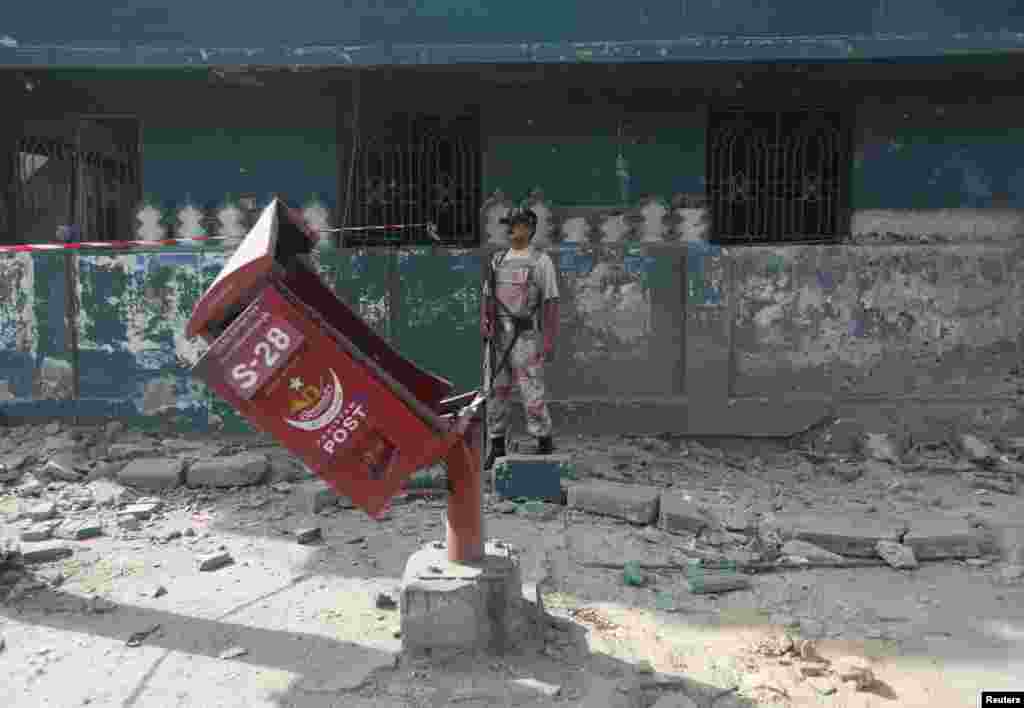 A paramilitary soldier stands near a damaged post box at the site of a bomb blast in Karachi, June 26, 2013.