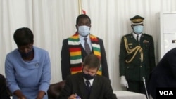 Andrew Pascoe (seated), the president of the Commercial Farmers Union of Zimbabwe, signs the agreement while President Emmerson Mnangagwa (with scarf) waits for his turn, at the State House in Zimbabwe, July 29, 2020. (Columbus Mavhunga/VOA) 