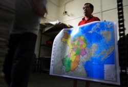 FILE - A worker holds a new officially approved map of China that includes the islands and maritime area that Beijing claims in the South China Sea, in May 2019 at a printing factory in Changsha in south China's Hunan province.